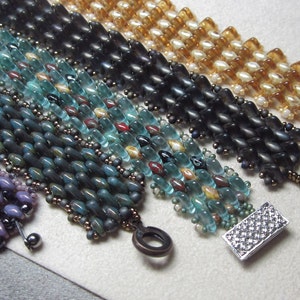 May include: A set of six beaded bracelets in various colors, including purple, teal, black, and brown. The bracelets are made with small, round beads and have decorative metal clasps.