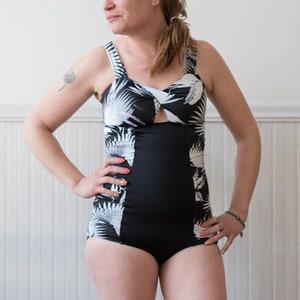 Op de afbeelding: Een zwart-witte badpak met een tropische bladerenprint. Het badpak heeft een hoge beenuitsnijding en een lage rug. Het badpak is gemaakt van een rekbare stof.