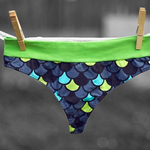 May include: Black and green underwear with a blue and green scale pattern. The underwear has a green waistband.