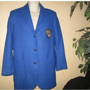 May include: A vibrant blue blazer with a classic design. The blazer features a three-button closure, two front pockets, and a patch on the chest. The patch has a colorful emblem. This jacket is a stylish addition to any wardrobe.