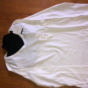 May include: White long-sleeve shirt with a V-neck and a black undershirt. The shirt has a tag that says "XS".