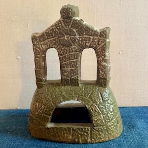 May include: A green ceramic turtle house with a textured surface and two arched openings. The house is designed to be a habitat for small animals.