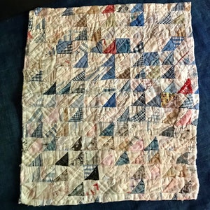 May include: A patchwork quilt made of small triangles in shades of blue, pink, white, and brown. The quilt is hand-stitched and has a vintage look.