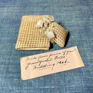 Puede incluir: Una pequeña bolsa de tela beige y un estuche cuadrado a juego con un estampado de puntos y un cierre de lazo. Una nota manuscrita dice: "Hecho con trozos del chaleco de boda de tu abuelo."