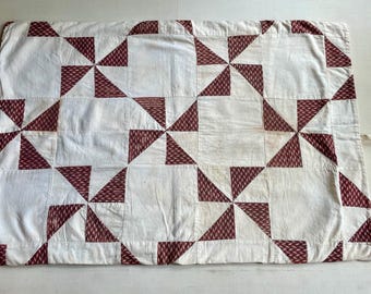 May include: A white quilt with a red and white geometric pattern. The quilt is made of squares with a pinwheel design in the center of each square.