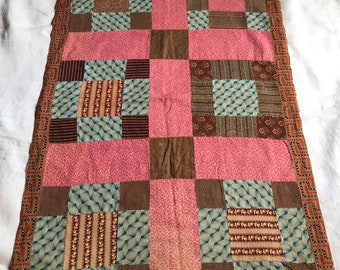 May include: A patchwork quilt with a pink, brown, and blue color scheme. The quilt is made of squares of different fabrics, each with a unique pattern. The quilt is bordered with a brown and white patterned fabric.