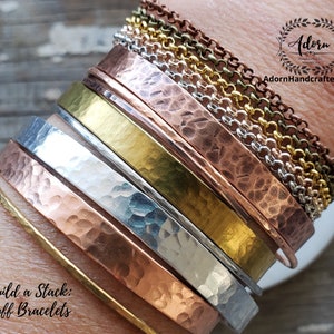 May include: A stack of hammered metal cuff bracelets in various colours, including copper, silver, and gold. The bracelets are arranged in a graduated size, with the largest at the bottom and the smallest at the top. The text "Build a Stack: Cuff Bracelets" is visible at the bottom of the image.