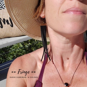 Könnte beinhalten: Eine Frau trägt einen breitkrempigen Strohhut und ein lila Oberteil mit einer schwarzen Halskette. Sie trägt lange schwarze Fransen-Suede-Ohrringe. Der Text "== Fringe == SUEDE EARRINGS: 4 COLORS" ist auf ihrer Schulter sichtbar.
