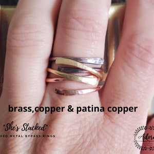 May include: A set of three mixed metal bypass rings in brass, copper, and patina copper. The rings are stacked on a finger and are labeled "She's Stacked" and "Mixed Metal Bypass Rings".