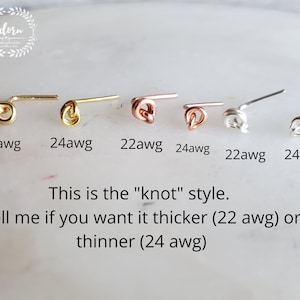 Peut inclure: Gros plan sur six petits clous d'oreilles en forme de nœud, en or, or rose et argent. Le texte indique les tailles de calibre : 22awg et 24awg. Le texte dit : "C'est le style "nœud". Dites-moi si vous le voulez plus épais (22 awg) ou plus fin (24 awg)"