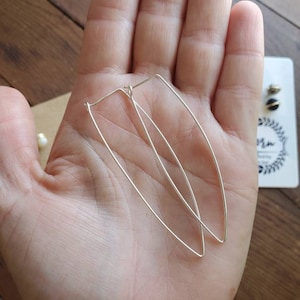 Könnte beinhalten: Ein Paar silberne Ohrringe in Form eines länglichen Ovals. Die Ohrringe sind schlicht und elegant.