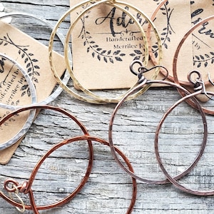 May include: Three pairs of hammered metal hoop earrings in silver, gold, and copper. The earrings are handcrafted by Merrilee Joy.