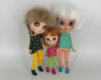 Könnte beinhalten: Drei Puppen in bunten Outfits mit Sternenmustern. Die Puppen haben langes Haar und tragen Strumpfhosen. Die Puppe links trägt einen grün-gelben Pullover, die Puppe in der Mitte trägt einen pink-grünen Pullover und die Puppe rechts trägt einen pink-blauen Pullover.