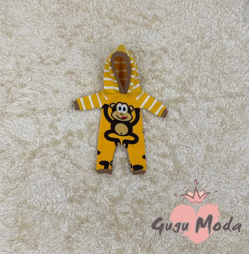 May include: Yellow knitted baby onesie with a monkey design and a brown striped hood.