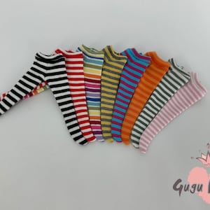 Op de afbeelding: Een verzameling kniehoge sokken in verschillende kleuren en gestreepte patronen. De sokken bevatten zwart-witte, rood-witte en oranje-blauwe strepen. De sokken zijn gerangschikt op een wit oppervlak.
