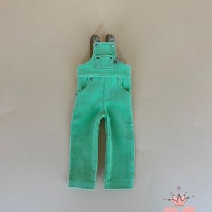 May include: A pair of bright green corduroy overalls with adjustable straps and pockets. The overalls have a classic design with metal hardware and are suitable for children. The corduroy fabric has a ribbed texture.