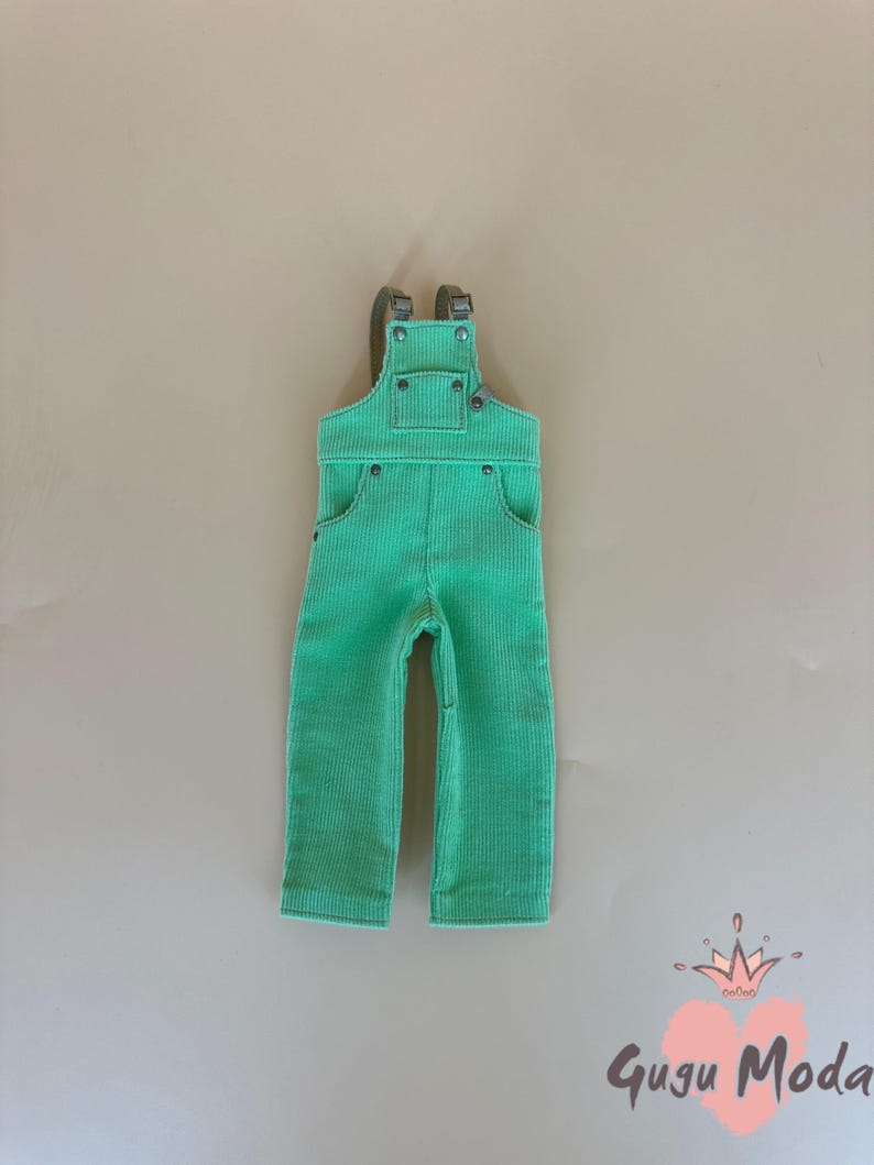 May include: A pair of bright green corduroy overalls with adjustable straps and pockets. The overalls have a classic design with metal hardware and are suitable for children. The corduroy fabric has a ribbed texture.