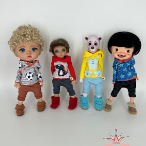 May include: Four dolls wearing different outfits. The dolls are wearing hoodies with various patterns, including a dinosaur, an anchor, and stars. The dolls are also wearing pants and boots.
