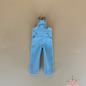 May include: Light blue corduroy overalls with adjustable straps and pockets. The overalls have a classic design with metal hardware and are suitable for children. The overall is displayed on a neutral background.