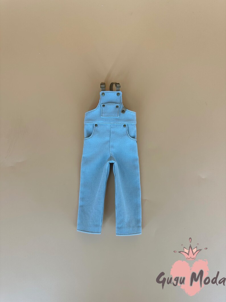 May include: Light blue corduroy overalls with adjustable straps and pockets. The overalls have a classic design with metal hardware and are suitable for children. The overall is displayed on a neutral background.