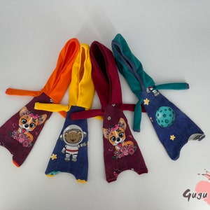 May include: Four hooded doll outfits with different patterns. One is red with a floral design and a dog, one is blue with a space theme, one is yellow with a space theme, and one is orange with a floral design and a dog.
