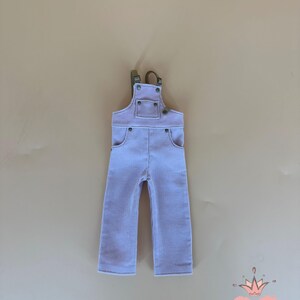 May include: Light purple corduroy overalls with adjustable straps and pockets. The overalls have a classic design with metal hardware. The Gugu Moda logo is in the bottom right corner.