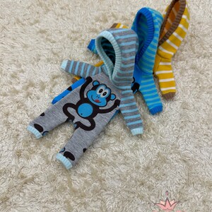 May include: Three striped hooded baby onesies with a monkey graphic. The onesies are in blue, yellow, and gray.