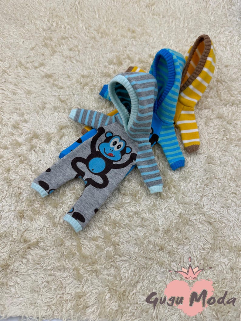 May include: Three striped hooded baby onesies with a monkey graphic. The onesies are in blue, yellow, and gray.