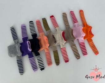 Puede incluir: Un conjunto de nueve suéteres de muñeca a rayas en varios colores, incluyendo gris, morado, negro, naranja, rosa, marrón y rojo. Los suéteres tienen mangas largas y están hechos de una tela suave y de punto.