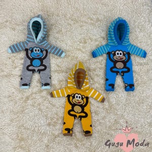 May include: Three baby onesies with a monkey design. The onesies are gray, blue, and yellow with a striped hood.