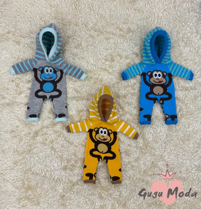 May include: Three baby onesies with a monkey design. The onesies are gray, blue, and yellow with a striped hood.