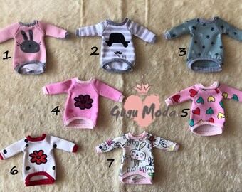 Peut inclure: Sept pulls différents pour poupées, de couleurs vives et avec des motifs variés, dont un lapin, une fleur, des cœurs et une moustache. Les pulls sont tous à manches longues et ont une bordure côtelée. Les pulls sont numérotés de 1 à 7.