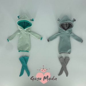 May include: Two doll-sized hooded sweatshirts with contrasting colored trim and matching leggings. One set is teal with white polka dots and the other is gray with white polka dots.