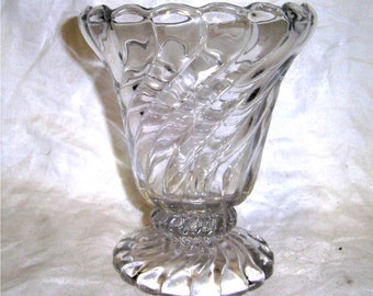 May include: A clear glass vase with a swirling, textured design. The vase has a wide, scalloped rim and a flared base.