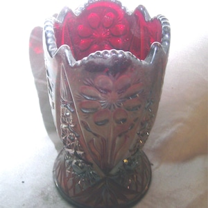 May include: A red glass vase with a floral pattern. The vase has a wide mouth and a flared base.