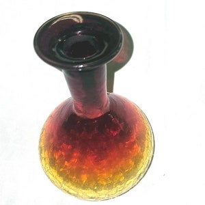 May include: A glass vase with a round body and a narrow neck. The vase is made of clear glass with a red, orange, and yellow ombre effect. The glass has a textured surface.
