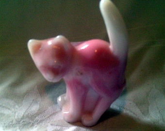 May include: A pink and white glass figurine of a cat. The cat is sitting with its tail curled up behind it.