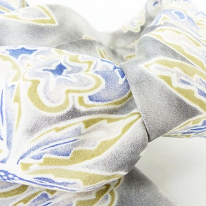 May include: A gray and white patterned fabric with blue and yellow floral designs. The fabric is folded in a way that shows the pattern.