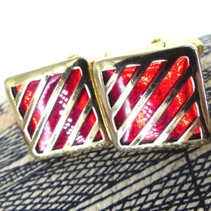 May include: A pair of gold cufflinks with red enamel and a striped design.