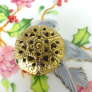 May include: Gold metal decorative button with a circular, openwork design. The button has a raised, textured surface and a delicate, intricate pattern.
