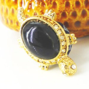 Cool little black and gold turtle lapel pin with rhinestone eye. Wear as a tie tack or hat pin. Magnetic MagTAK. Silk covered back button