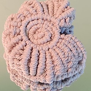 Puede incluir: Un posavasos de macramé beige claro con un diseño en espiral en el centro. El posavasos es redondo y presenta un patrón tejido texturizado. El macramé está hecho de una gruesa y suave cuerda de algodón.