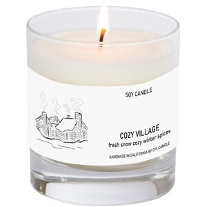 K&ouml;nnte beinhalten: Eine wei&szlig;e Sojawachskerze in einem durchsichtigen Glasgef&auml;&szlig; mit einer Schwarzwei&szlig;illustration eines Hauses mit Rauch aus dem Schornstein. Das Etikett lautet "SOY CANDLE", "COZY VILLAGE", "fresh snow cozy winter spices" und "HANDMADE IN CALIFORNIA BY CHI CANDLE".