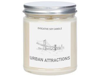 May include: A white soy candle with a silver lid. The label features a black and white illustration of a bridge and cityscape with the text "Evocative Soy Candle" and "Urban Attractions".