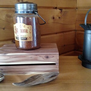 May include: A glass jar with a metal lid and handle filled with brown cinnamon. The jar is sitting on a wooden crate. A black metal candle holder with a pineapple design is on the right side of the image.