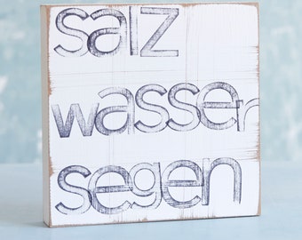 May include: White wooden sign with black lettering that reads "Salz Wasser Segen".
