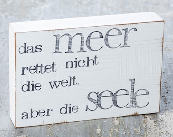 May include: White wooden sign with black text that reads "das meer rettet nicht die welt, aber die seele"