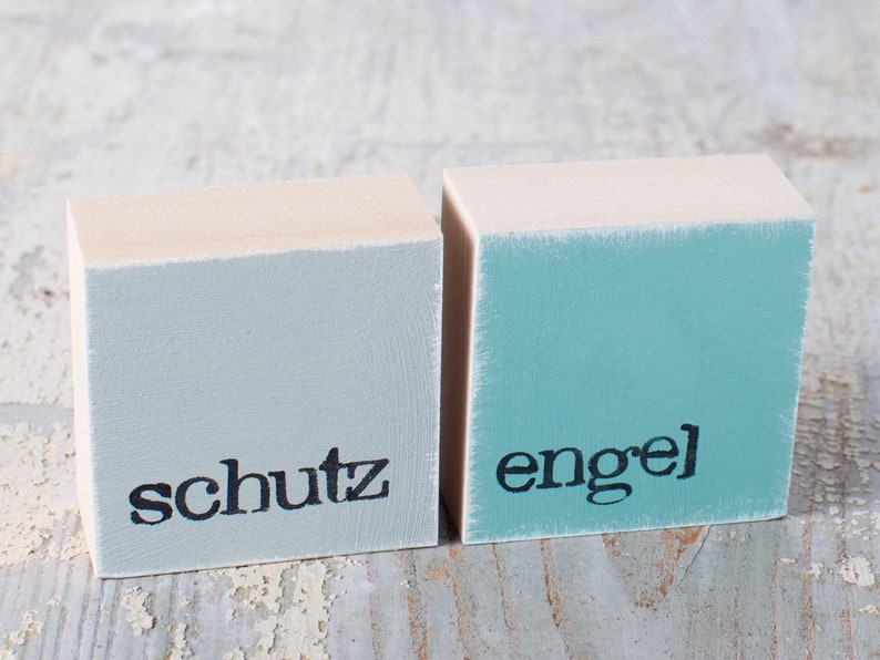 May include: Two wooden blocks painted in light blue and turquoise with the words "schutz" and "engel" painted in black.