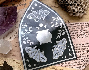 Mirror Sticker Witchin'. Cathedral portal shape with magical cauldron, triple moon, and three moths in black, gray, and silver colors.