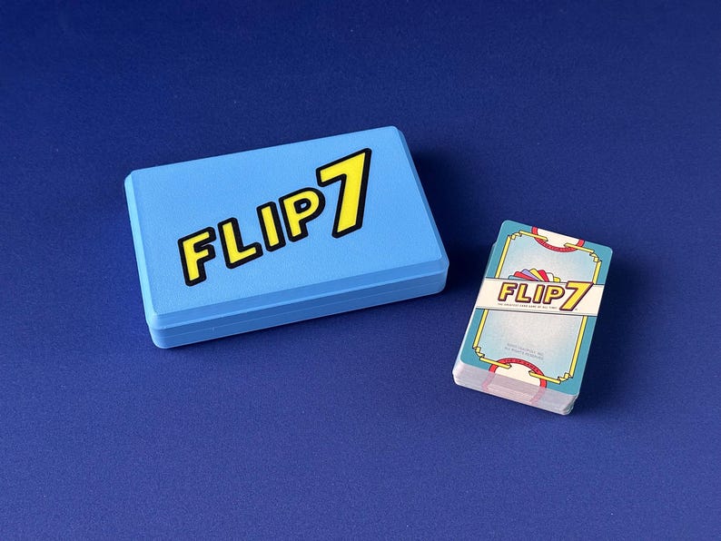 Puede incluir: Una caja de juego azul claro y una baraja de cartas sobre una superficie azul. La caja y las cartas presentan el texto "FLIP 7" en amarillo con un contorno negro. Las cartas tienen un borde decorativo.